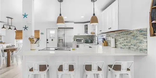 Image 3: Kitchen featuring a white countertop island with integrated cooktop, pendant lighting, stainless steel refrigerator, white cabinetry, and a mosaic tile backsplash