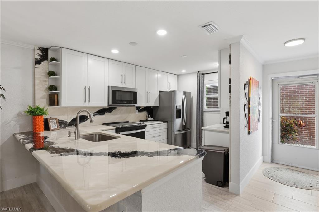Image 2: Kitchen featuring white cabinetry, stainless steel appliances, a bar-height counter with integrated sink, recessed lighting, and a patterned backsplash