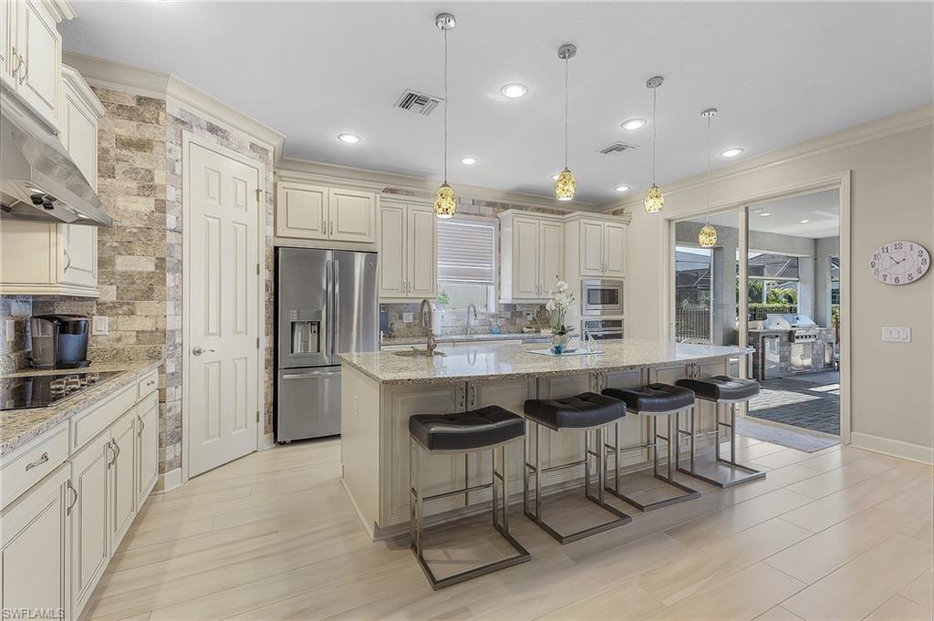 Image 3: Spacious kitchen featuring an expansive central island with seating, pendant lighting, stainless steel appliances, and light-toned cabinetry
