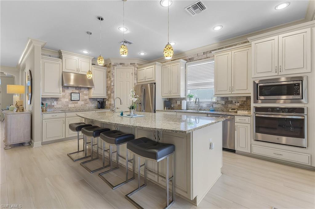 Image 4: Spacious kitchen featuring an expansive center island with seating, granite countertops, light-toned cabinetry, stainless steel appliances, and wood-finish flooring