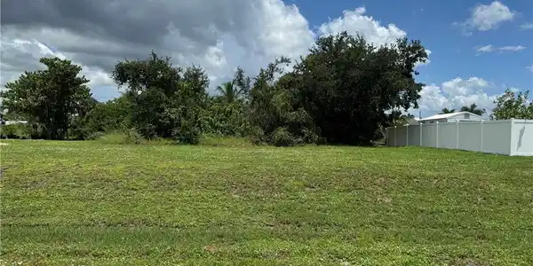 Image 3: Expansive lot featuring a manicured lawn, established landscaping, and a white vinyl privacy fence