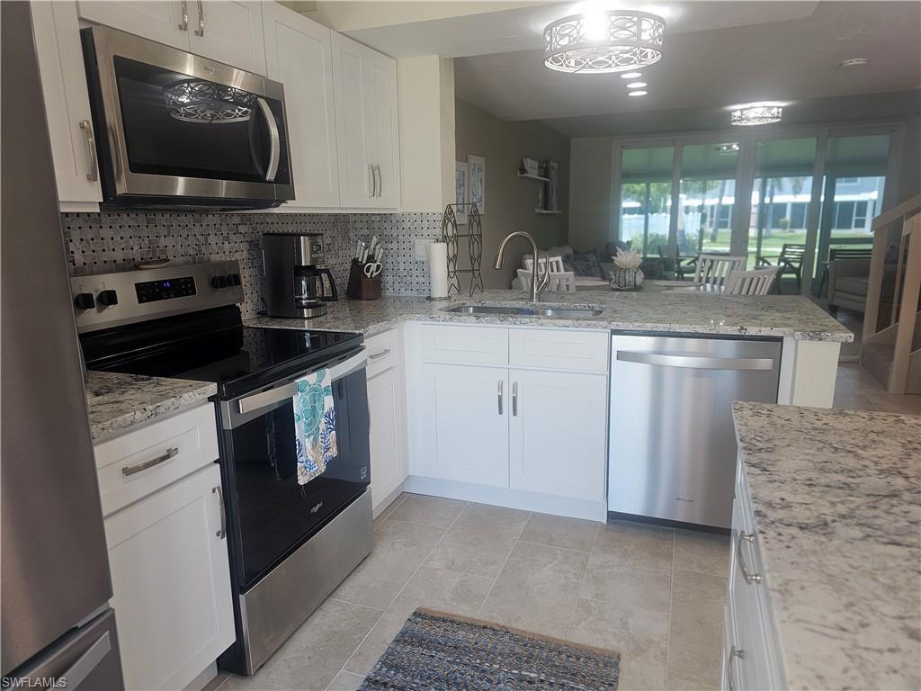 Image 4: Kitchen featuring stainless steel appliances, backsplash, a peninsula, white cabinets, and light stone counters