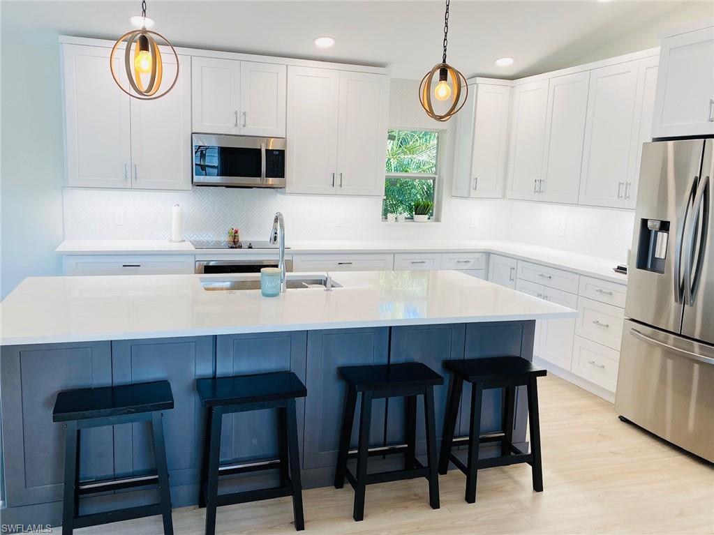 Image 2: Kitchen with stainless steel appliances, white cabinets, pendant lighting, light wood-style floors, and a kitchen island with sink