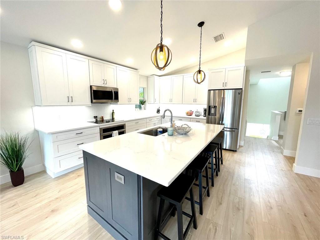 Image 3: Kitchen with white cabinets, appliances with stainless steel finishes, a breakfast bar area, a kitchen island with sink, and decorative light fixtures
