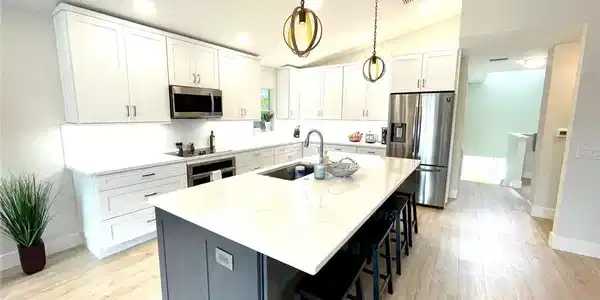 Image 3: Kitchen with white cabinets, appliances with stainless steel finishes, a breakfast bar area, a kitchen island with sink, and decorative light fixtures