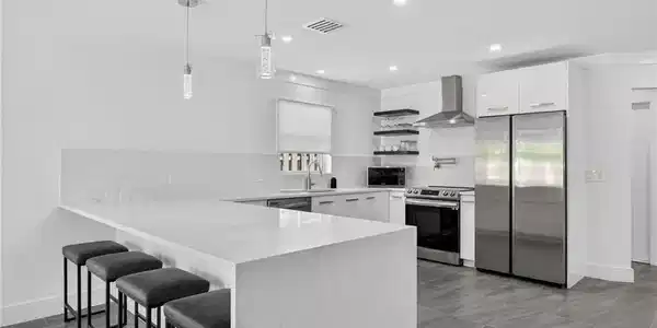 Image 2: Kitchen featuring open shelves, a breakfast bar area, appliances with stainless steel finishes, decorative backsplash, and white cabinetry