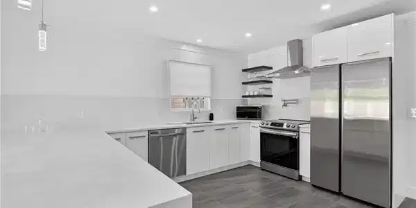 Image 3: Kitchen featuring open shelves, stainless steel appliances, white cabinetry, wall chimney range hood, and light stone counters