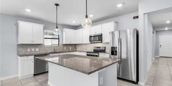Image 3: Kitchen featuring stainless steel appliances, granite counters, pendant lighting, white cabinetry, and a center island