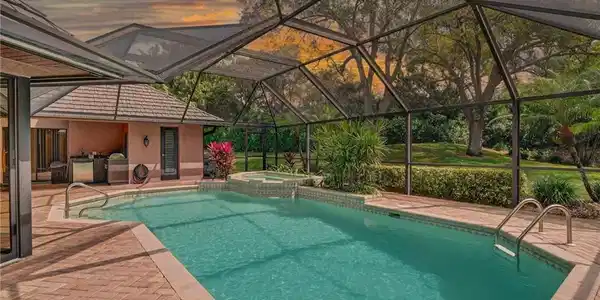 Image 2: Pool at dusk featuring a lanai, a sunroom, a pool with connected hot tub, and a patio