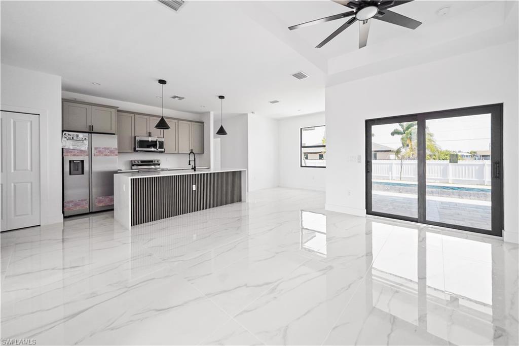 Image 3: Open-concept living area featuring large format polished tile flooring and a kitchen island with a slatted wood-finish panel