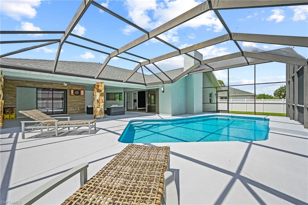 Image 4: Screened-in outdoor living space with a free-form swimming pool, extensive concrete decking, and a covered patio area