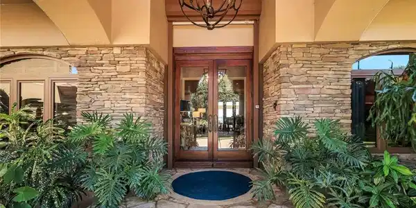 Image 3: Stacked stone facade with arched entryways and a wood-frame double-door entrance featuring glass panels
