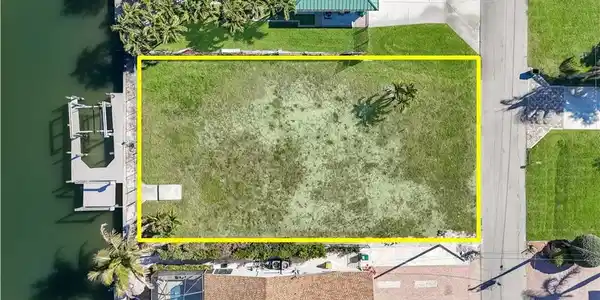 Image 4: Waterfront lot featuring a concrete boat dock with multiple slips, a grass lawn, and mature palm trees - Virtually Edited Image