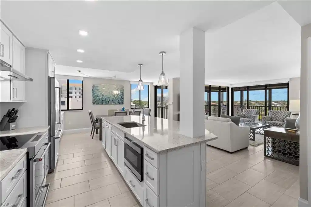 Image 1: Open-concept kitchen featuring an island with an undermount sink, stainless steel appliances, light cabinetry, and light-toned tile flooring