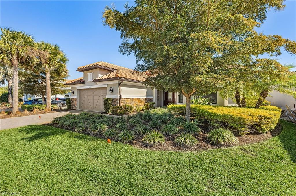 Image 3: View of front of property featuring a front yard, stucco siding, driveway, stone siding, and an attached garage