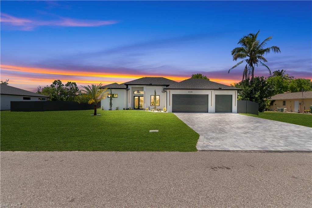 Image 1: Contemporary single-story residence featuring a white stucco facade, black shingle roof, and an expansive paver driveway