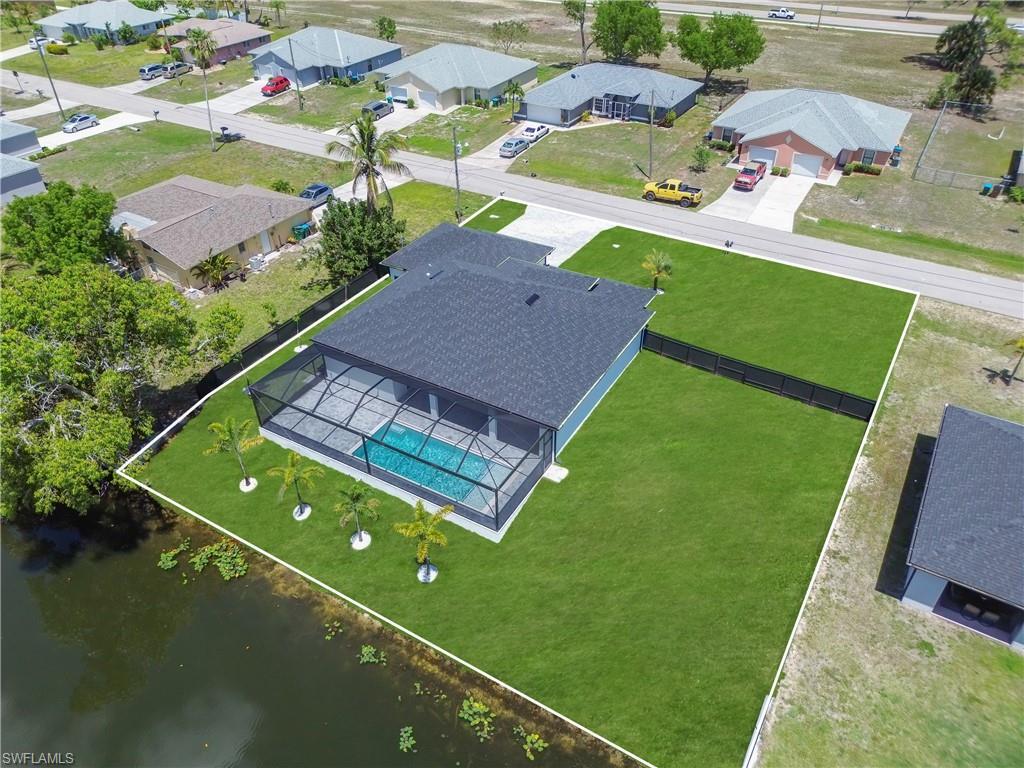 Image 2: Waterfront property featuring a screened-in pool enclosure, dark shingle roof, lush green lawn, and a black privacy fence