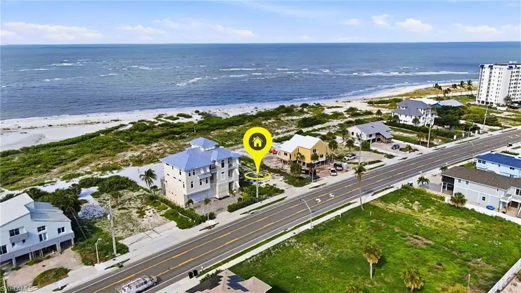 Image 1: Elevated coastal home featuring multiple balconies, a light blue metal roof, and direct beach proximity - Virtually Edited Image