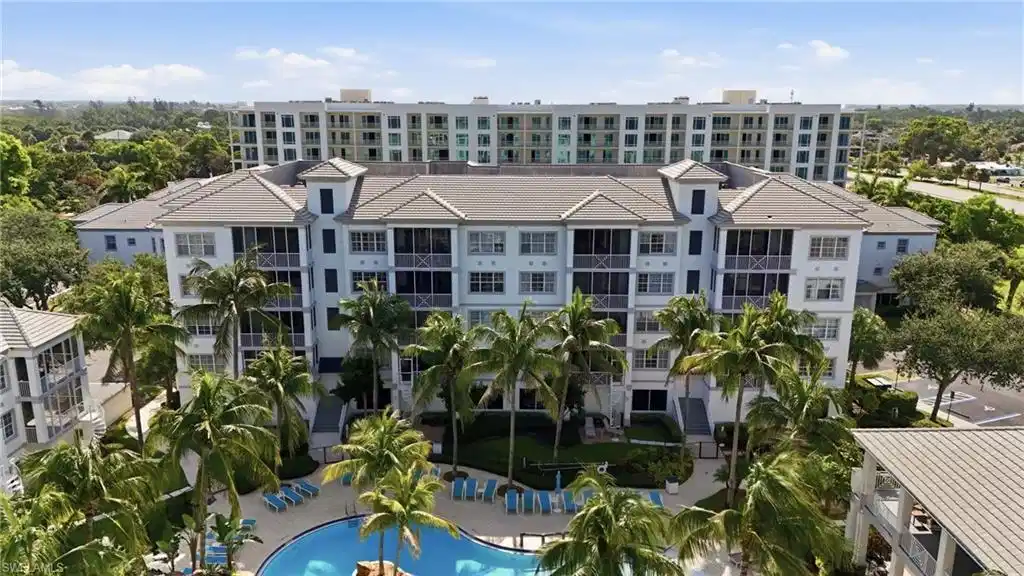 Image 1: Multi-story residential complex featuring screened balconies, a central swimming pool with lounge chairs, mature palm trees, and a light-colored exterior with gray roofs