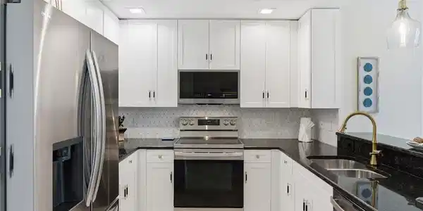 Image 4: U-shaped kitchen with white cabinetry, dark stone countertops, stainless steel appliances, a tile backsplash, and recessed lighting