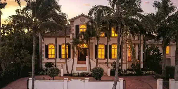Image 4: Stucco exterior with a tiled roof, arched windows, decorative shutters, and mature palm trees