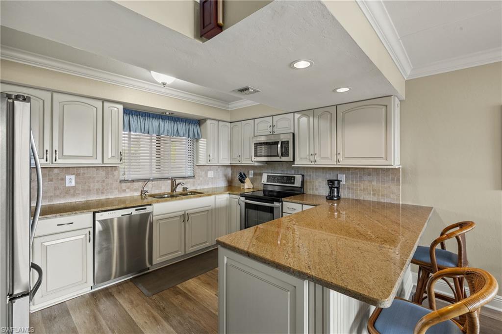 Image 4: Kitchen with appliances with stainless steel finishes, white cabinetry, sink, a kitchen breakfast bar, and kitchen peninsula