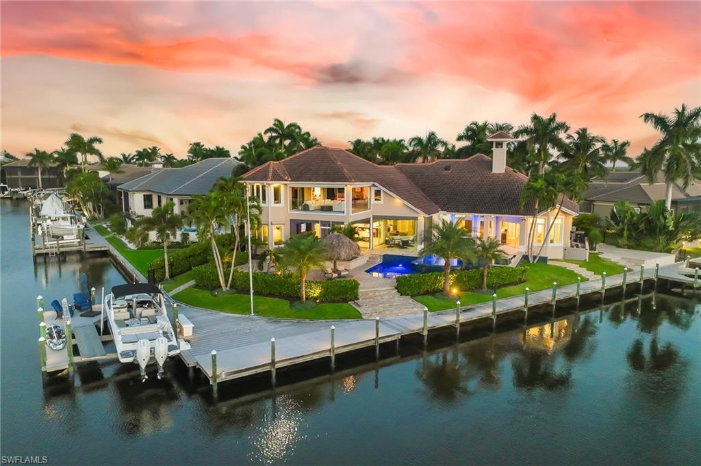 Image 1: Back of property at dusk featuring an outdoor pool, a water view, boat lift, a patio area, and a balcony