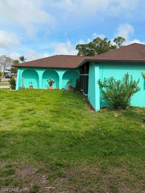 Image 3: View of home's exterior with stucco siding, a lawn, and roof with shingles