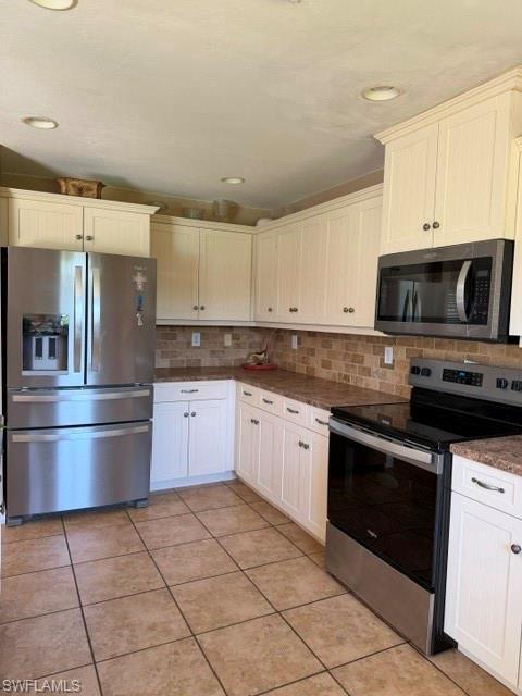 Image 4: Kitchen with stainless steel appliances, decorative backsplash, white cabinetry, light tile patterned flooring, and dark stone countertops