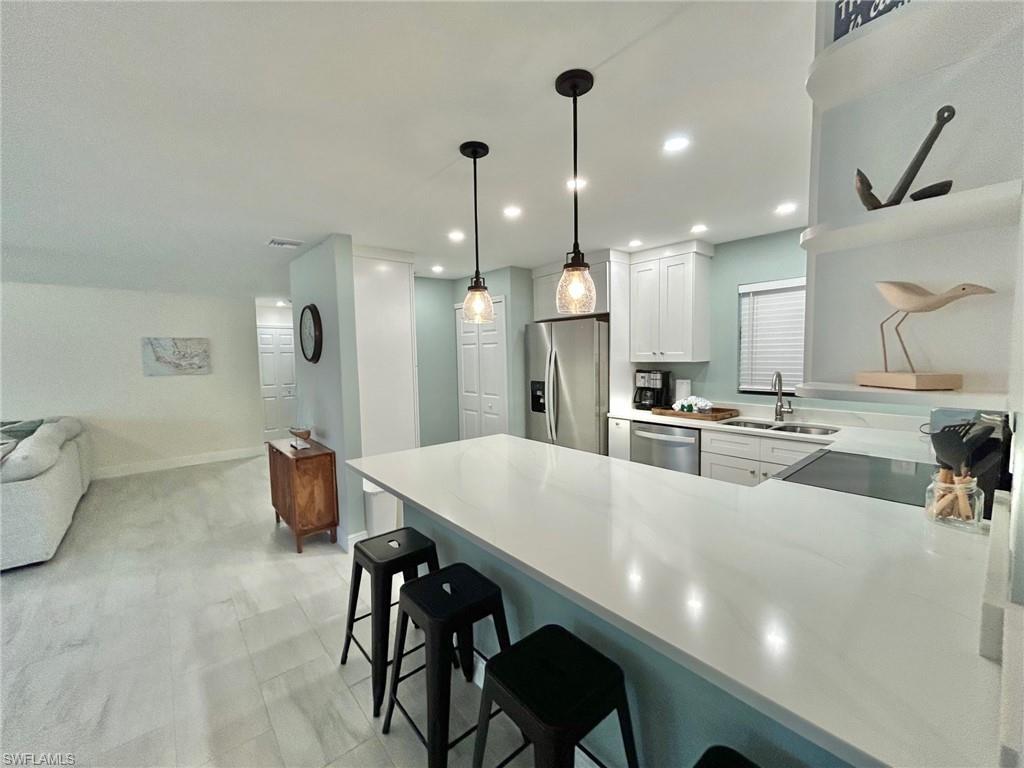 Image 4: Kitchen featuring a kitchen breakfast bar, a peninsula, stainless steel appliances, white cabinetry, and hanging light fixtures