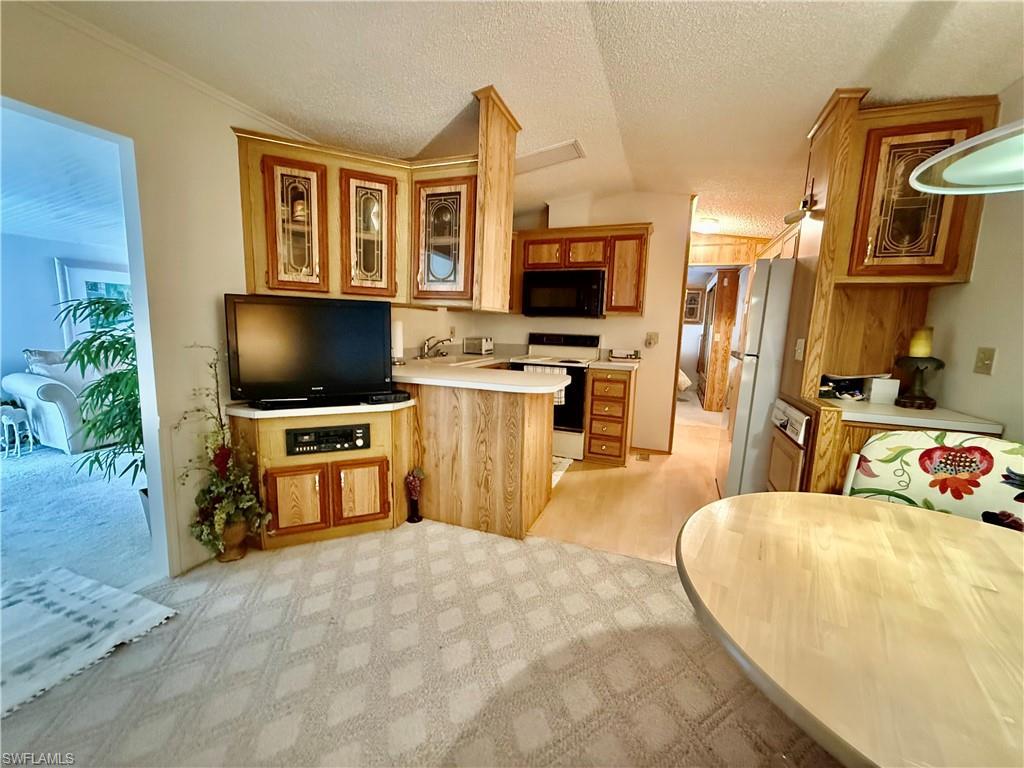 Image 4: Kitchen with light countertops, glass insert cabinets, white appliances, a peninsula, and light colored carpet
