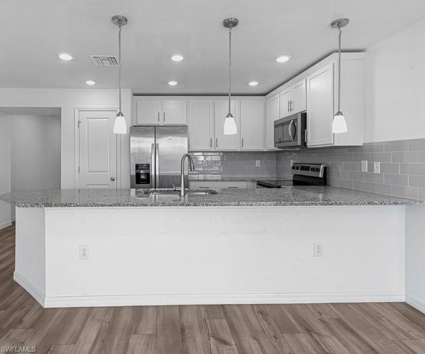 Image 3: Kitchen with a peninsula, light stone counters, stainless steel appliances, white cabinetry, and light wood-style flooring