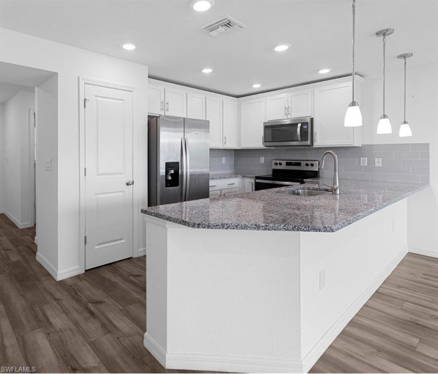 Image 4: Kitchen with dark stone counters, stainless steel appliances, a peninsula, white cabinetry, and light wood-style flooring