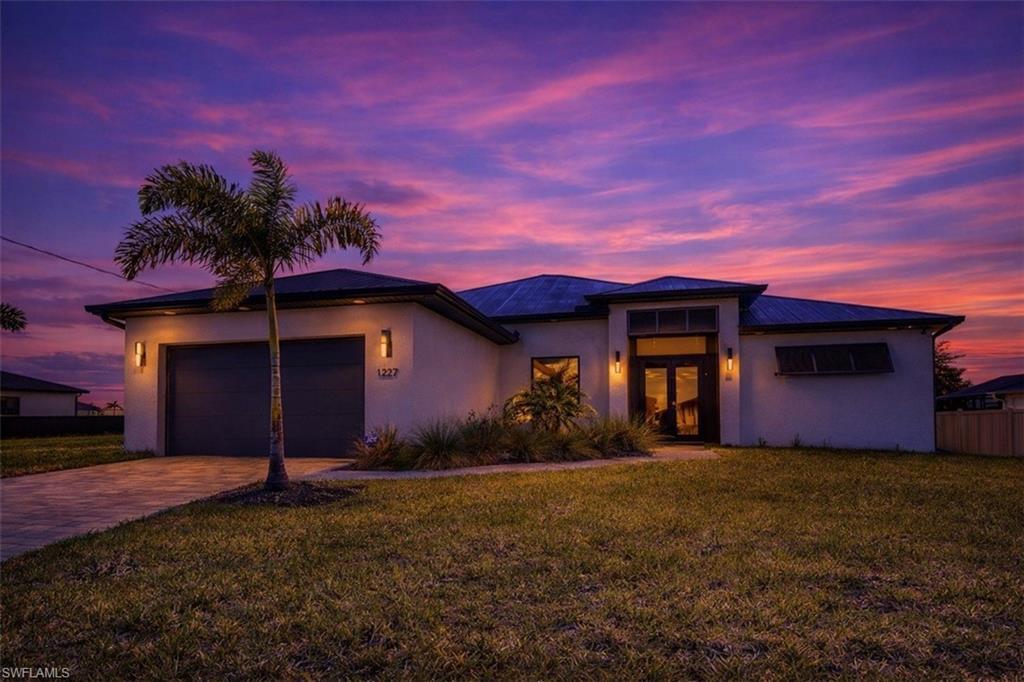 Image 1: View of front of property featuring a front lawn, a garage, driveway, stucco siding, and french doors