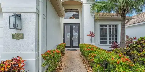 Image 2: Stucco exterior featuring a paver walkway bordered by maintained shrubs and landscaping