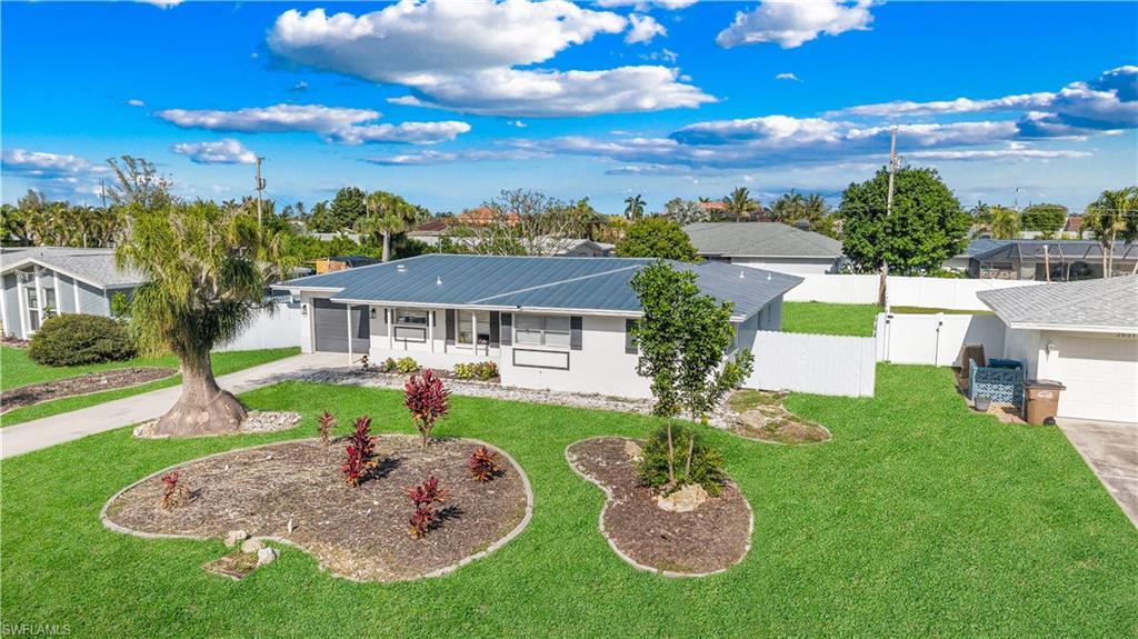 Image 3: The property features a well-maintained lawn, established landscaping beds, a paved driveway, and a white fence