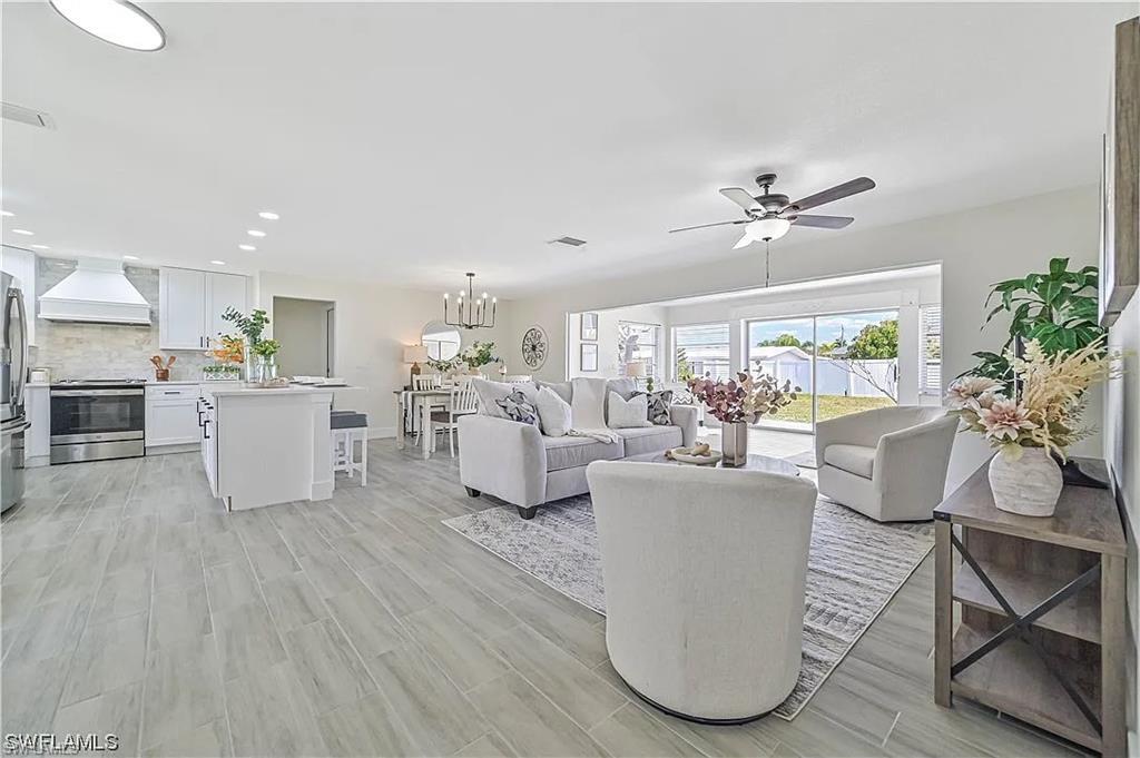 Image 4: Open concept living area featuring light-toned flooring, a kitchen with white cabinetry and stainless steel appliances, and a living room with a ceiling fan