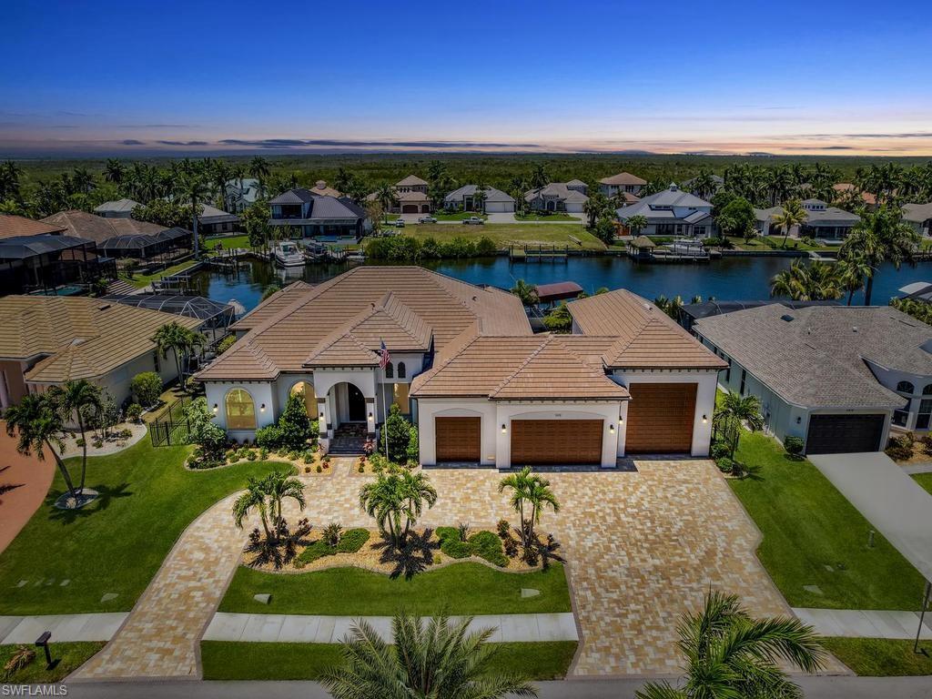 Image 1: Expansive waterfront residence featuring a barrel tile roof, paver driveway, three-car garage, and established landscaping
