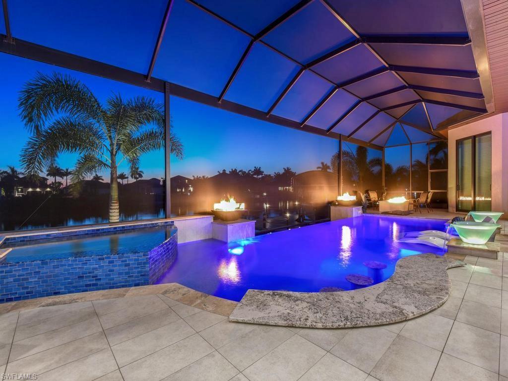 Image 4: Screened patio enclosure featuring a swimming pool with integrated seating, an elevated spa with blue mosaic tile, and a surrounding paver deck