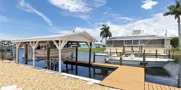 Image 4: Waterfront property featuring a covered boat lift, an additional boat slip, a wooden dock, and a gravel-covered bank