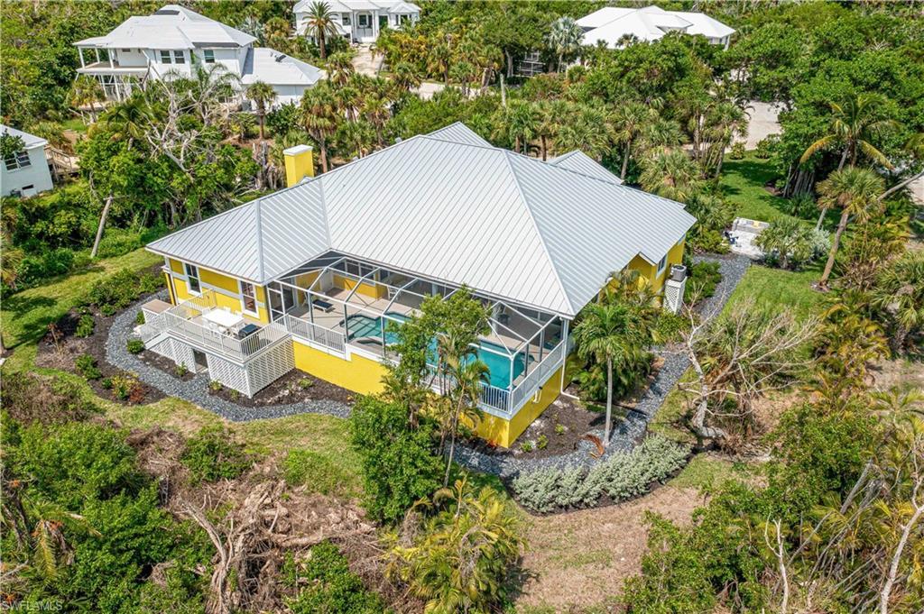 Image 2: Yellow exterior residence featuring a screened-in pool enclosure, a metal roof, an elevated deck, and surrounding landscaping with mature trees and shrubs