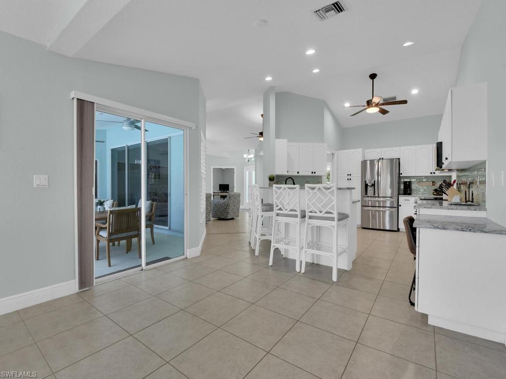 Image 4: Open-concept kitchen featuring white cabinetry, stainless steel appliances, and a central island with bar seating