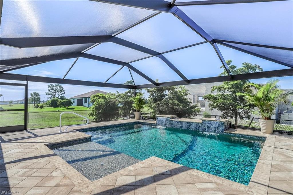 Image 3: Screened outdoor pool area featuring a blue-tiled swimming pool with integrated waterfall features, a shallow sun shelf, and a paver patio surround