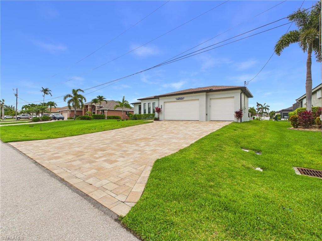 Image 2: Exterior featuring a three-car garage, an expansive paver driveway, and a well-maintained lawn