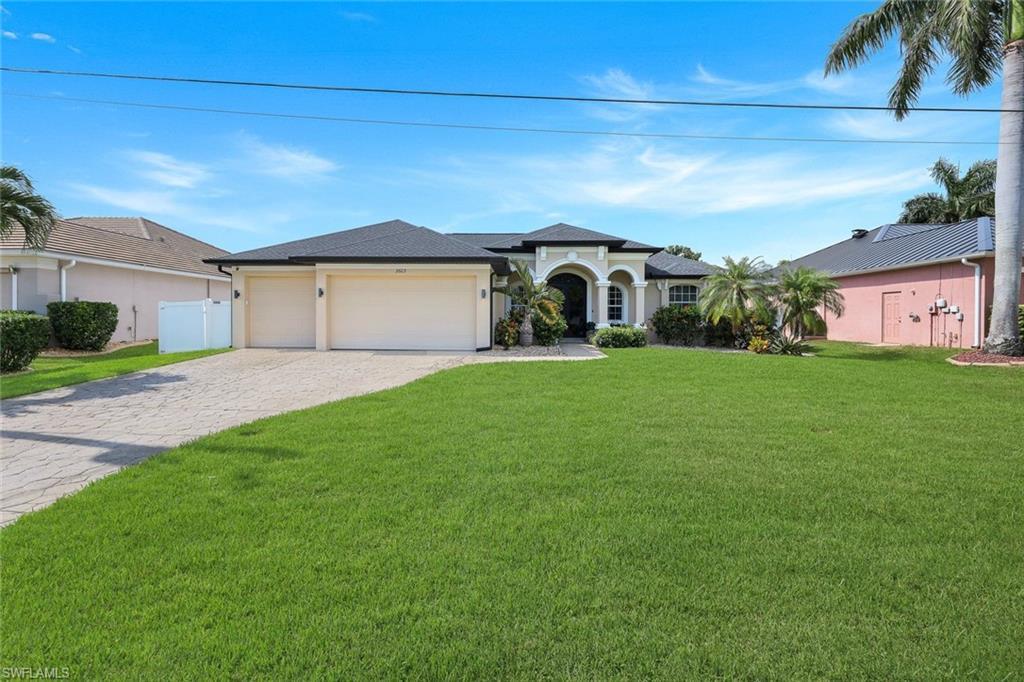Image 1: Cream-colored stucco exterior with a dark shingle roof, featuring an arched entry, a two-car garage, and a paver driveway