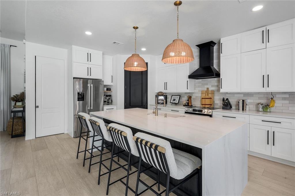 Image 2: Spacious kitchen featuring a large central island with seating, white shaker cabinetry, stainless steel appliances, and wood-finish flooring