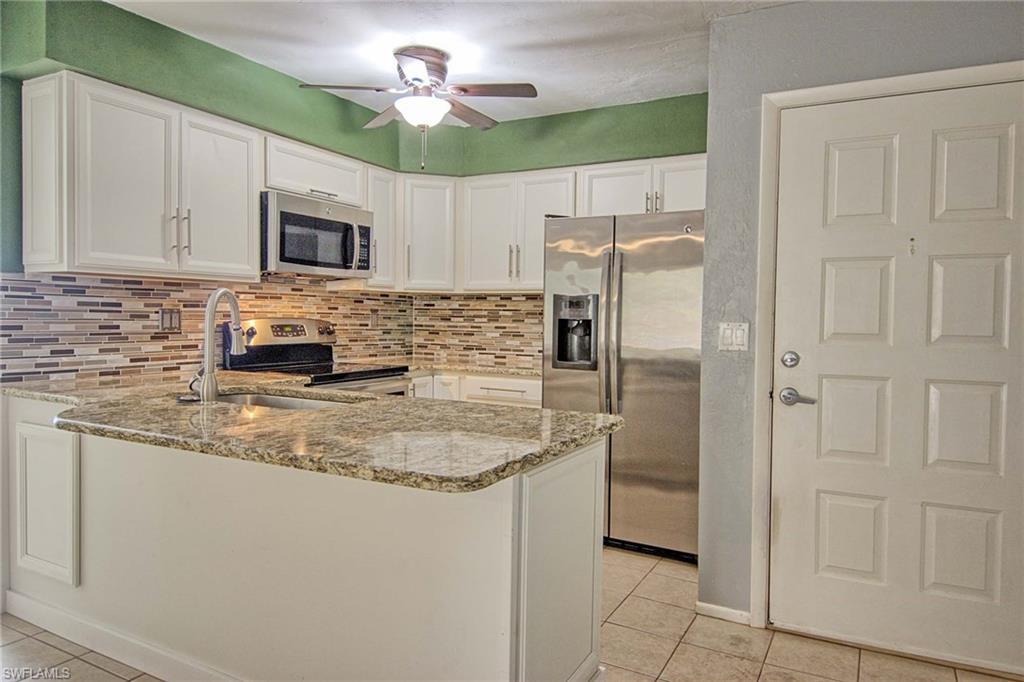 Image 2: Kitchen featuring white cabinetry, a granite countertop island with an undermount sink, a mosaic tile backsplash, and stainless steel appliances including a refrigerator, microwave, and range