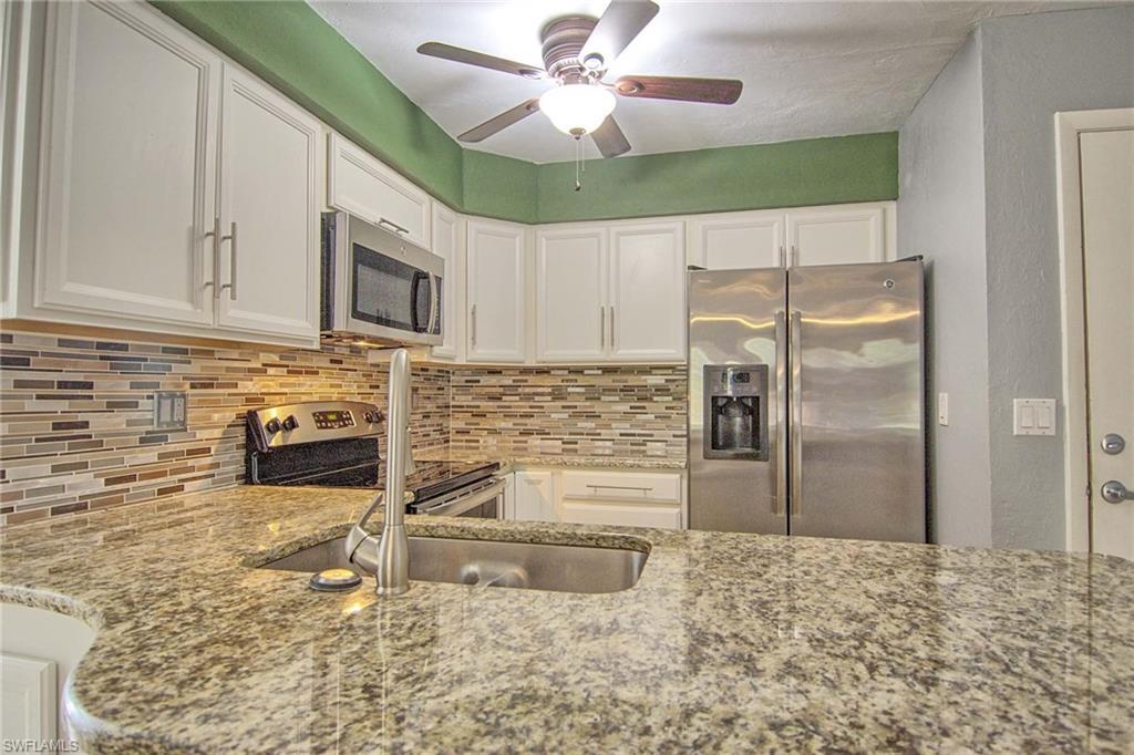 Image 3: Kitchen featuring granite countertops, stainless steel appliances, white cabinetry, a mosaic tile backsplash, and a ceiling fan