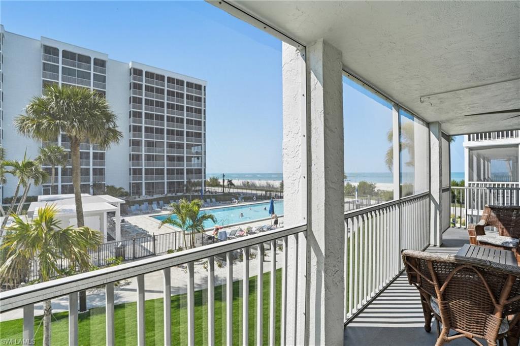 Image 3: Screened balcony overlooking a pool, manicured lawn, and beach