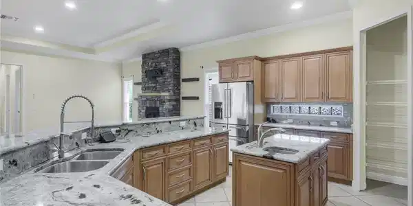 Image 3: Spacious kitchen featuring light wood cabinetry, stone countertops, a double basin sink, and a center island with an additional sink